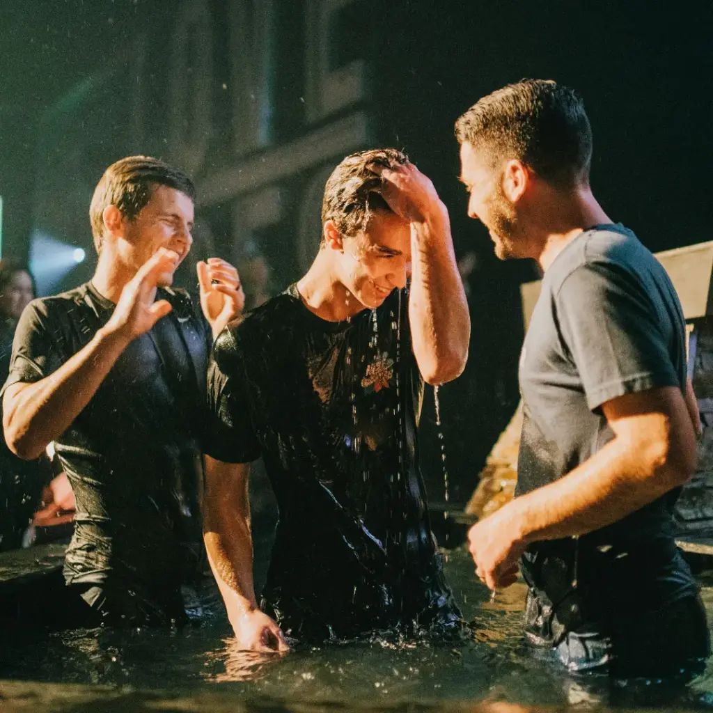 Young man being baptised in water by two smiling men, picturing what we mean by gospel saturated
